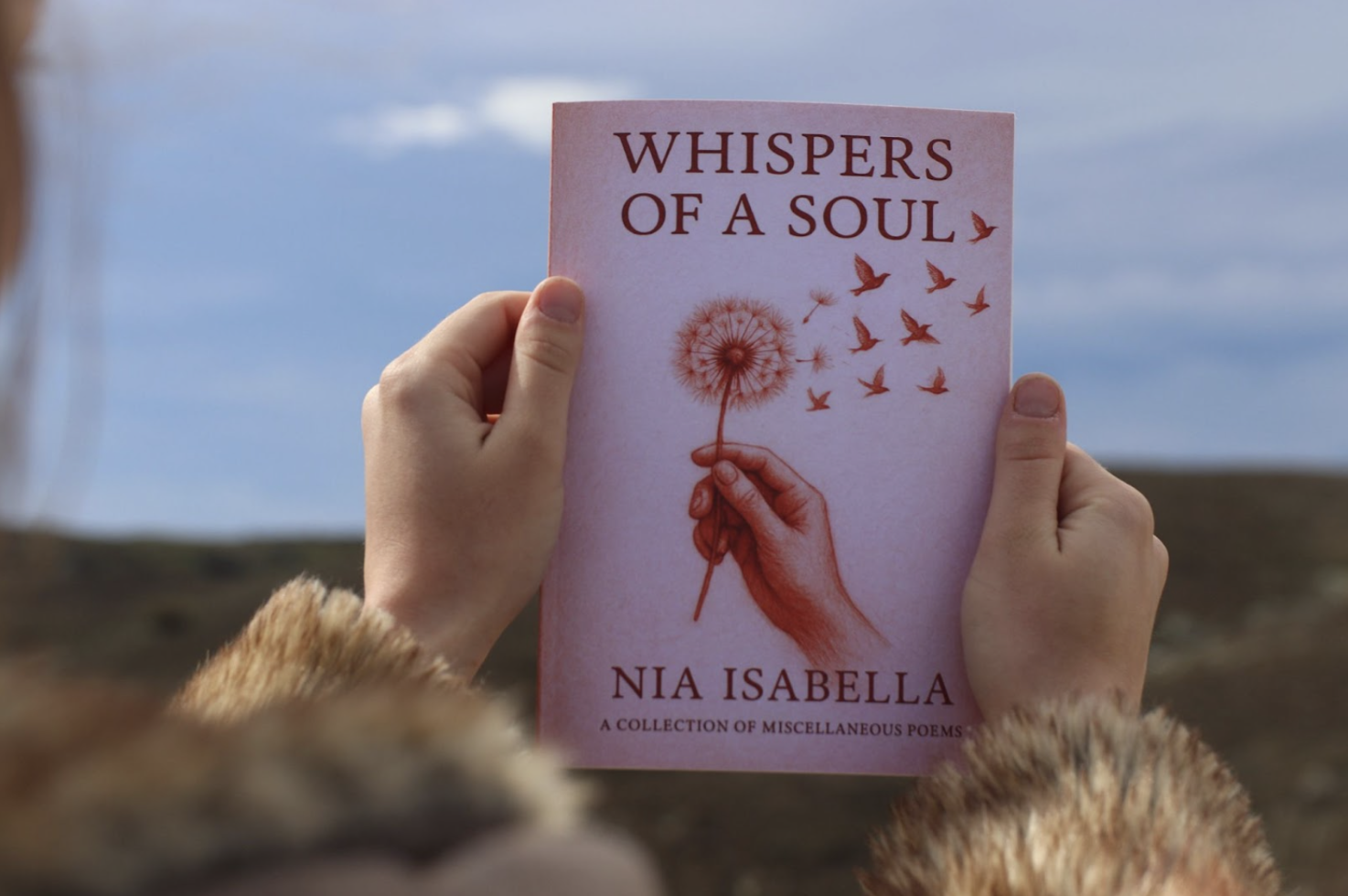 A person holding the book Whispers of a Soul by Nia Isabella outdoors